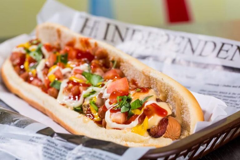 loaded hot dog with salsa and sauces placed on a plate lined with a newspaper