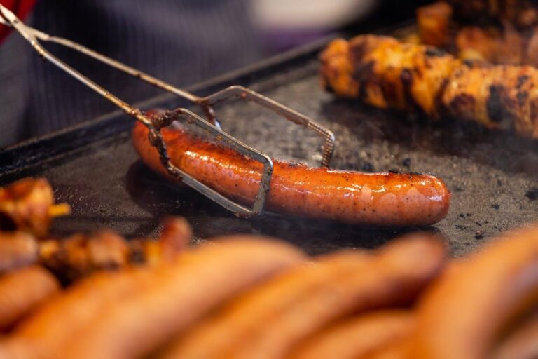 a sausage being held by tongs, sizzling while being cooked on a grill