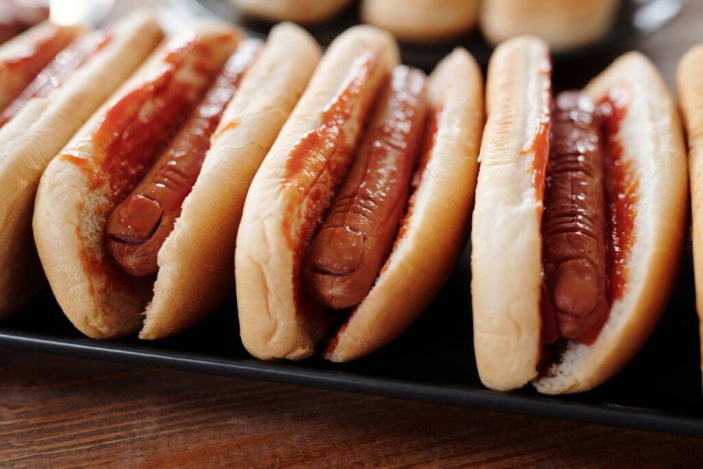 A close-up of grilled hot dogs with ketchup in soft buns, lined up for a backyard event.