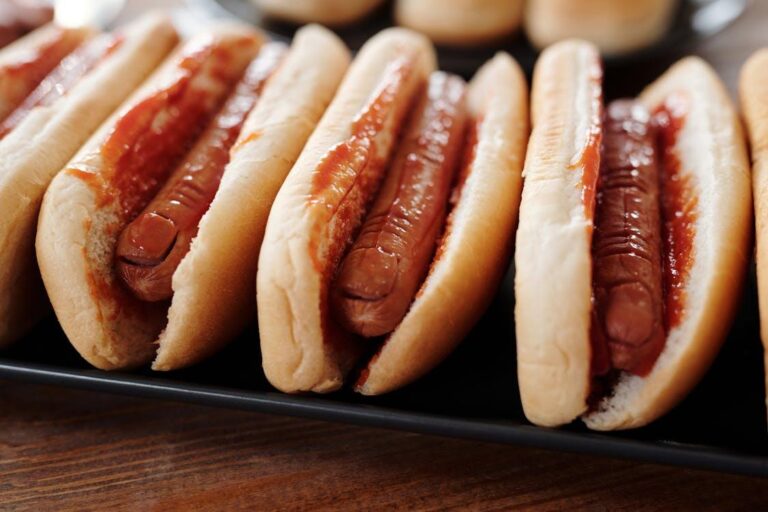 A close-up of grilled hot dogs with ketchup in soft buns, lined up for a backyard event.