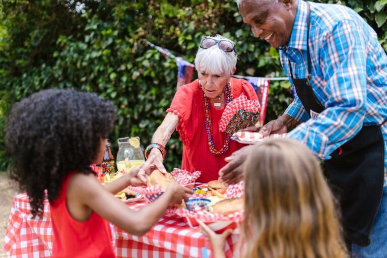 Multi-generational family enjoying hot dogs at a red-checkered picnic table during an outdoor event