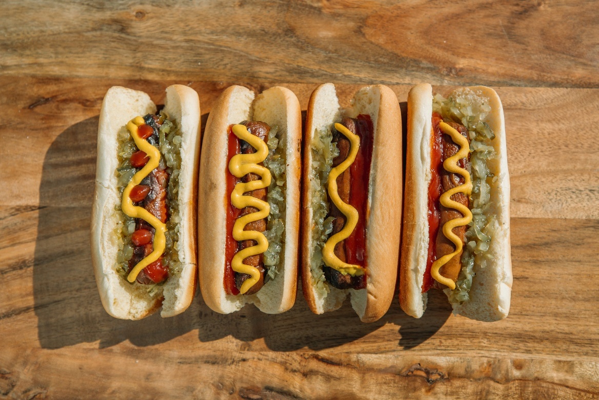 Five grilled hot dogs topped with mustard and relish, neatly arranged on a wooden table