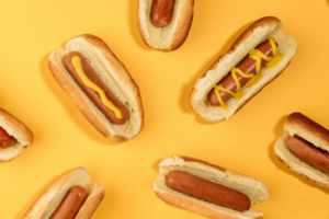 Assorted plain and mustard-covered hot dogs laid out on a yellow background