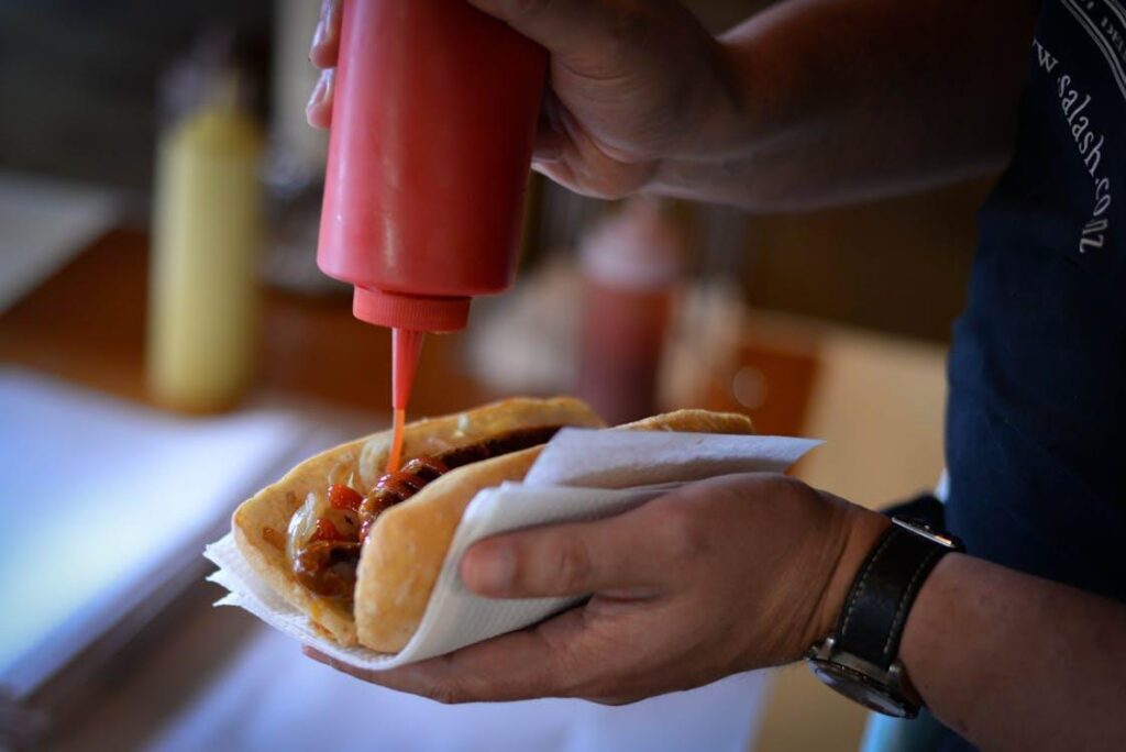 A person squeezes ketchup onto a hot dog while holding it with a napkin during contest prep