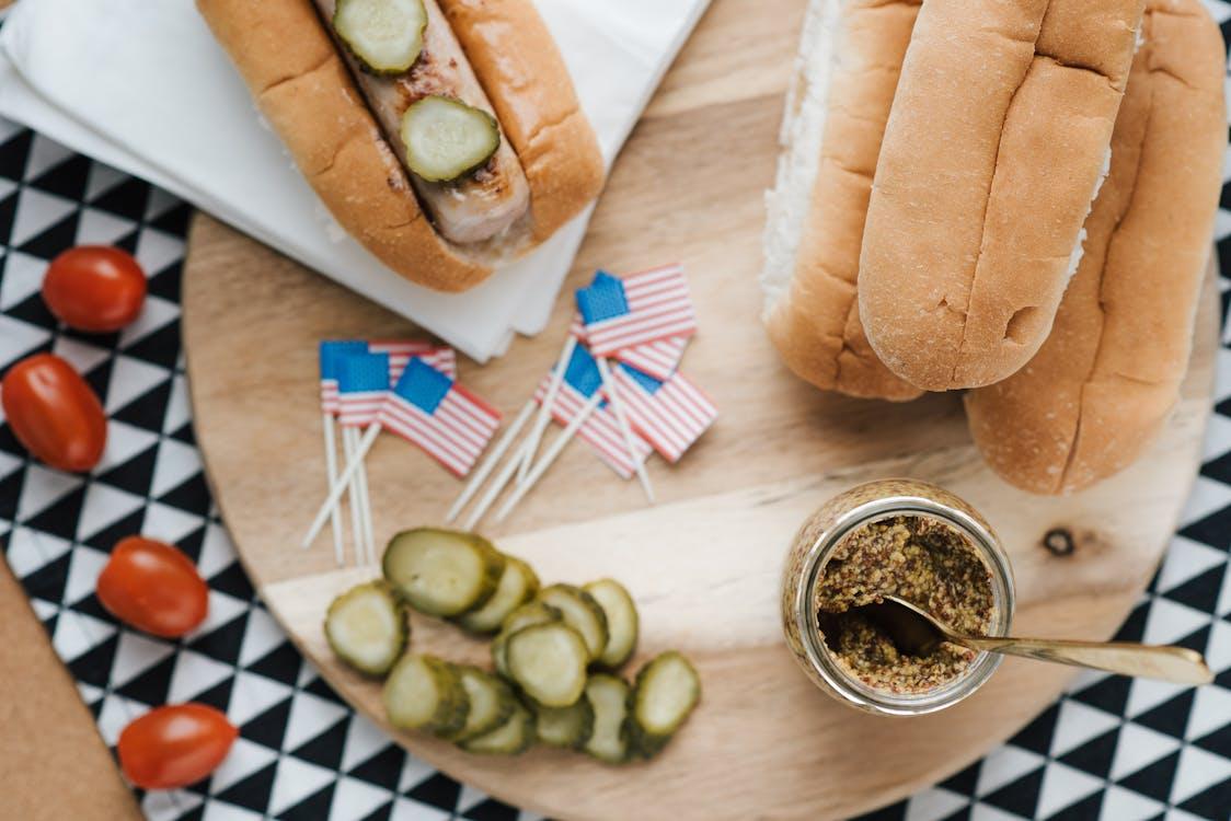 Hot dogs with pickles and mustard beside small American flags and condiments