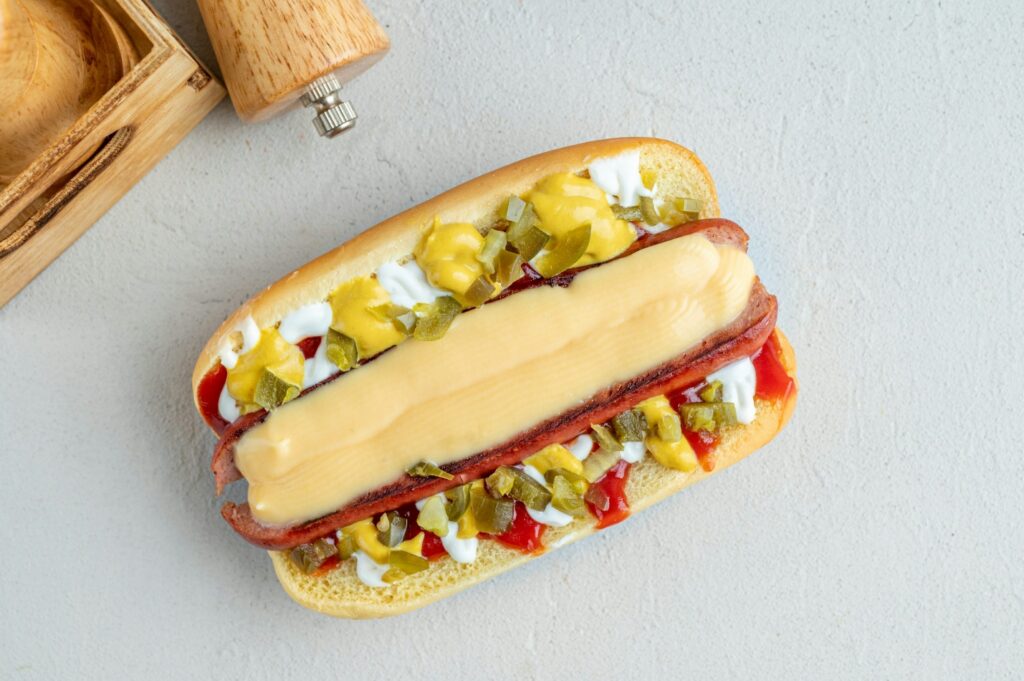 Melted cheese-topped hot dog with pickles, mustard, and ketchup for a perfect texture study