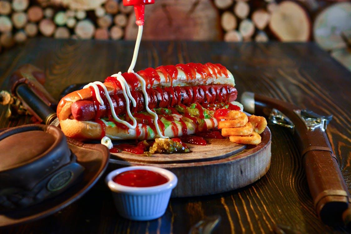 Double hot dog loaded with ketchup and mayo, drizzled on a rustic wooden table