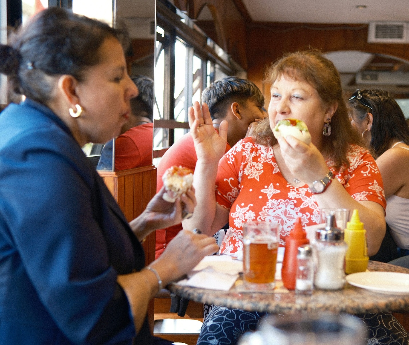 Two women laughing and eating hot dogs together at a casual diner