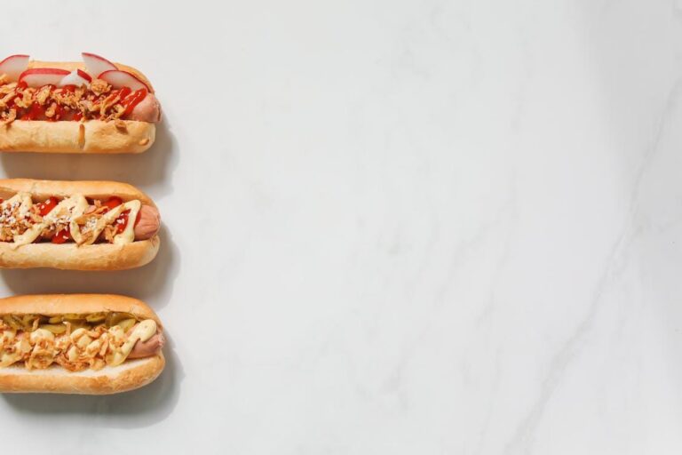 Three gourmet hot dogs on a marble counter with creative toppings for a festival feature