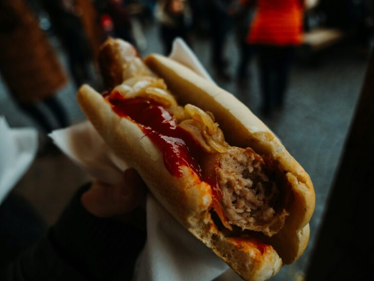 Close-up of a partially eaten hot dog with ketchup and onions held at a street event