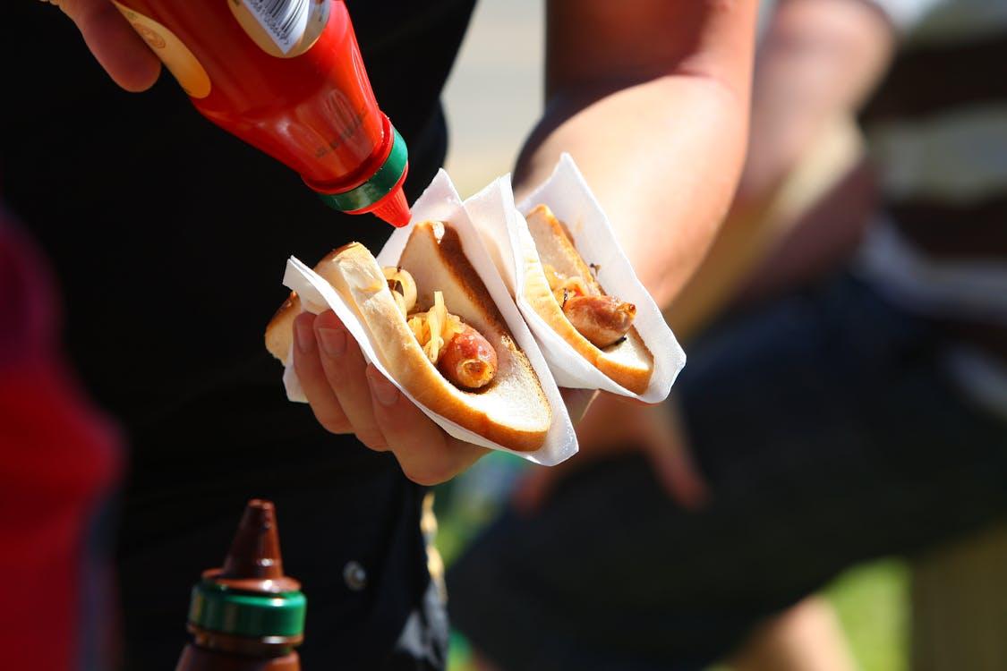 Person holding two festival-style hot dogs with mustard and onions